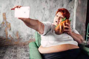 Fat woman with sandwich in hand makes selfie, laziness and obesity, overweight people. Unhealthy lifestyle, fatty female