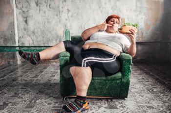 Fat woman sits in a chair and eats sandwich, overweight, fatty and  bulimic. Unhealthy lifestyle, obesity