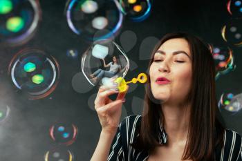 Young woman blows colorful soap bubbles, black background. Female person blowing colorful balloons