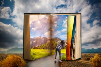 Little woman turns the page of large book, desert valley, blue sky with clouds on background, scale effect. Gaining knowledge and education, reading concept.