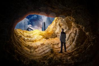 Businessman standing in a cave and looks on skyscrapers at the end. Business success search concept