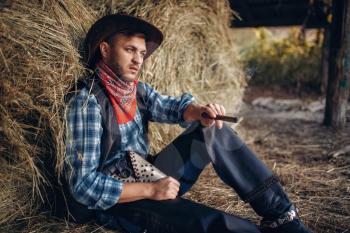Brutal cowboy relax with cigar, haystack on background, western. Vintage male person with gun on farm, wild west culture
