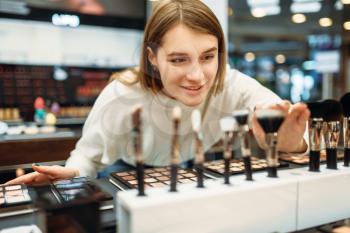 Female customer choosing brushes in the makeup shop. Cosmetics choosing in beauty store, make-up