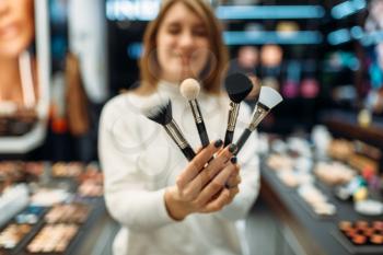 Female seller shows brushes in the makeup shop. Cosmetics choosing in beauty store, make-up