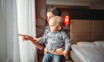 Young mother with little male child looks out the window. Mom and son happy together at home, togetherness