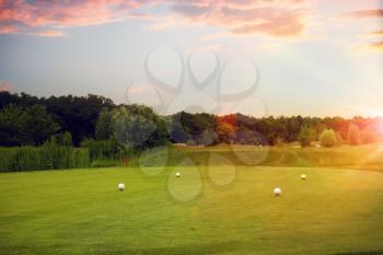 Four white balls on golf course, launching point, nobody. Green meadow in sport club at sunset, trimmed lawn for game, playground