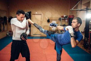 Male kickboxer practicing kicking with a personal trainer, workout in gym. Boxer strikes on training, kickboxing practice