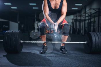 Male powerlifter in sportswear rubs his hands with talcum powder, preparation for exercise with barbell in gym. Weightlifting workout, powerlifting training, lifter works with weight in sport club