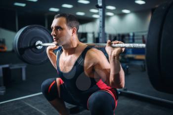 Muscular powerlifter doing squats with barbell in gym. Weightlifting workout, powerlifting training in sport club