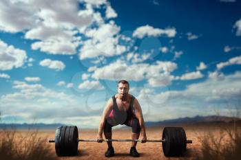 Male weightlifter prepares to take weight, deadlift, sandy desert on background. Weightlifting workout outdoor, bodybuilding training