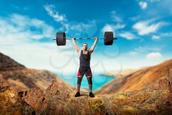Strong weightlifter takes a weight on the top of mountain, deadlift, sea or ocean on background. Weightlifting workout outdoor, bodybuilding training