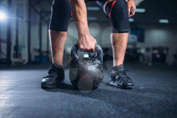 Strong male athlete prepares for exercise with kettlebell lifting. Weightlifting workout in sport or fitness club, weight lifter on training in gym