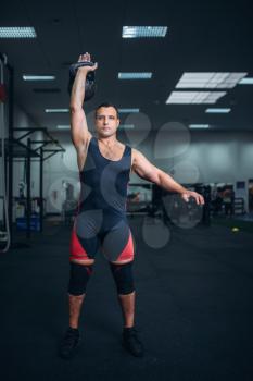 Strong man in sportswear doing exercise with kettlebell, weight lifting. Weightlifting workout, athlete in sport or fitness club, lifter on training in gym