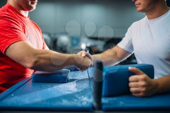 Two arm wrestlers shake hands after battle or wrestling competition, gym interior on background. Wrestle challenge, power sport
