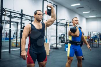 Strong male athletes with weights in gym, kettlebell lifting. Weightlifting workout in sport or fitness club