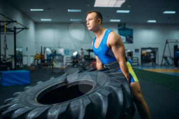 Strong male athlete doing strength exercise with truck tyre in gym, crossfit workout. Cross fit training in sport club