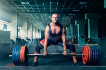 Male weightlifter prepares to pull heavy barbell, deadlift, gym interior on background. Weightlifting workout in sport or fitness club, bodybuilding