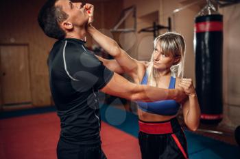 Female person on self-defense workout with male personal trainer, gym interior on background. Woman makes punch to the throat on training, self defense practice