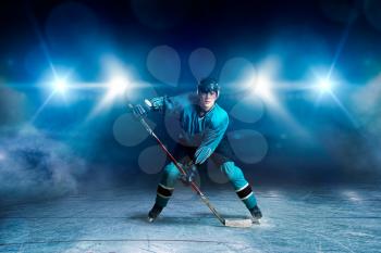 Hockey player with stick on ice, game concept, spotlights on dark background. Male person in helmet, gloves and uniform, extreme sport