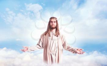 Jesus Christ in white robe standing with open arms against cloudy sky. Son of God, christian faith