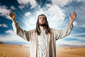 Jesus Christ in white robe praying with his hands up against cloudy sky. Strong faith in God, christianity