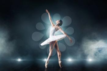 Ballet dancer in white dress dancing on the stage in theatre. Graceful ballerina training in class