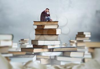 Man sits on a stack of books. Lots of books around. Gaining knowledge and education concept. Student reading