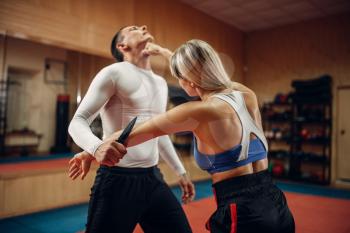 Woman makes punch to the throat, self-defense workout with male personal trainer, gym interior on background. Female person on training, self defense practice