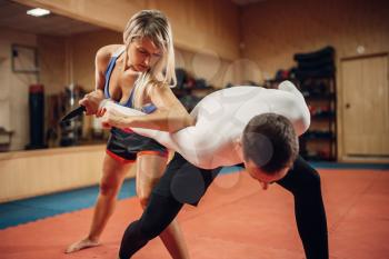 Woman makes elbow kick, self-defense workout with male personal trainer, gym interior on background. Female person on training, self-defense practice