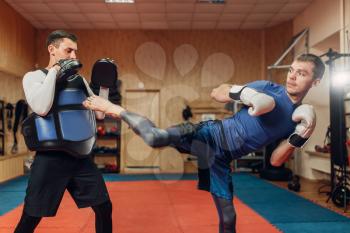 Male kickboxer practicing kicking with a personal trainer, workout in gym. Boxer strikes on training, kickboxing practice