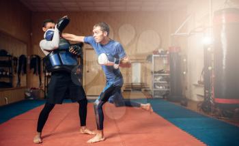 Male kickboxer in gloves practicing hand punch with a personal trainer in pads, workout in gym. Boxer on training, kickboxing practice