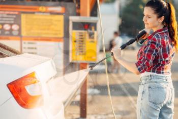 Cute woman with car washer on self service carwash. Outdoor vehicle washing at summer day. Female person with high pressure water gun