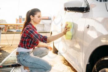 Young woman with sponge scrubbing vehicle with foam, car wash. Lady on self-service automobile washing. Outdoor carwash at summer day 