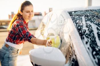 Female person hand with sponge scrubbing vehicle with foam, car wash. Young woman on self-service automobile washing. Outdoor carwash