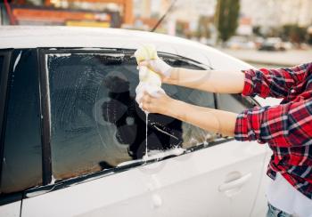 Female person with sponge scrubbing vehicle window with foam, car wash. Young woman on self-service automobile washing. Outdoor carwash at summer day 