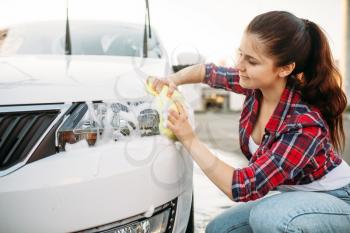Female person with sponge cleans vehicle headlight, car wash. Young woman on self-service automobile washing. Outdoor carwash at summer day
