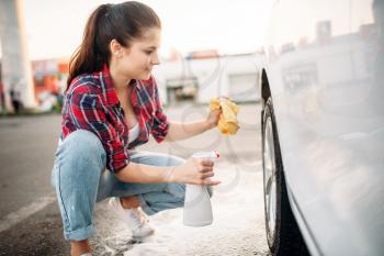 Woman cleans wheel disk of the car with spray, carwash. Lady on self-service automobile washing. Outdoor vehicle cleaning at summer day 
