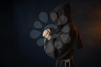 Medieval monk in black robe with hood praying with closed eyes, secret ritual. Mysterious friar in dark cape. Mystery and spirituality