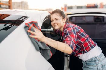 Woman wipes automobile after washing on self-service car wash. Lady cleaning vehicle