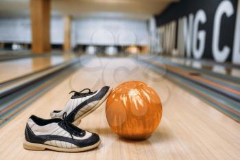 Bowling ball and house shoes on wooden floor in club, pins on background, nobody. Bowl game concept, tenpin
