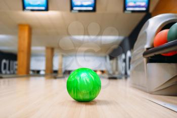 Green bowling ball on wooden floor in club, closeup view, nobody. Bowl game concept