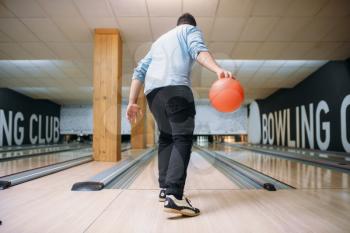 Male bowler standing on lane and poses with ball in hands, back view. Bowling alley player prepares to throw strike shot in club, active leisure