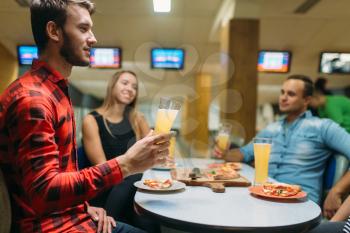 Friends drinks juice and eats pizza in bowling club, active leisure, healthy lifestyle, bowl game