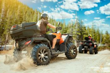 Two quad bike riders in helmets travels in forest. Riding on atv, extreme sport and travelling, quadbike adventure