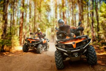 Two atv riders in helmets, speed race in forest, front view. Riding on quad bike, extreme sport and travelling, quadbike offroad adventure