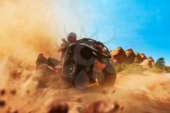 Quad bike rider climbing the sands in quarry, front view, dust clouds. Male driver in helmet on atv, offroad in sandpit