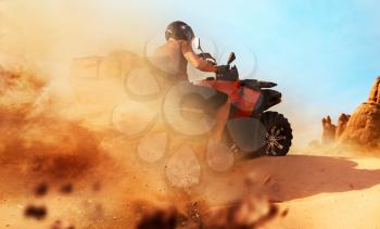 Atv riding in sand quarry, dust clouds. Male driver in helmet on quad bike, extreme freeriding on quadbike in desert dunes