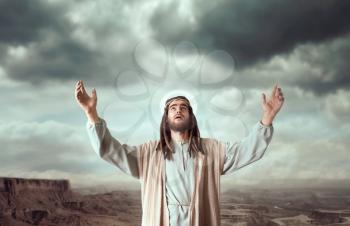 Jesus Christ in white robe praying with his hands up against cloudy sky. Strong faith in God, christianity