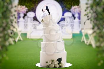 Wedding cake with bride and groom figures on the top, marriage proposal. Sweet pie for newlyweds with little figurines