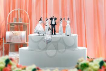 Wedding cake, groom and many brides figurines on the top. Dummy pie for newlyweds with little figures